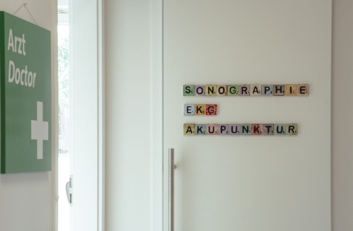 Der Praxisflur mit grünem Arztschild und bunten Holzbuchstaben an der Wand