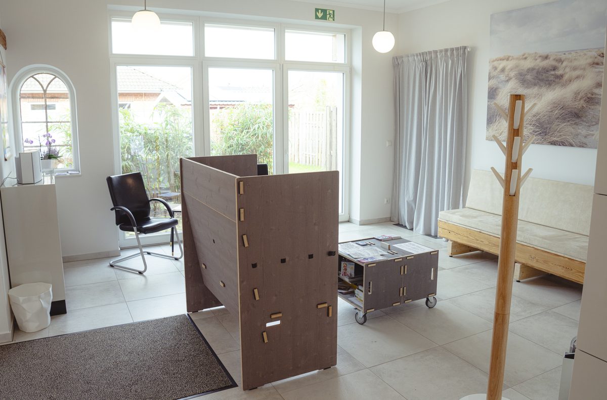 Der Wartebereich mit Sitzbank, Garderobe und großen Fenstern